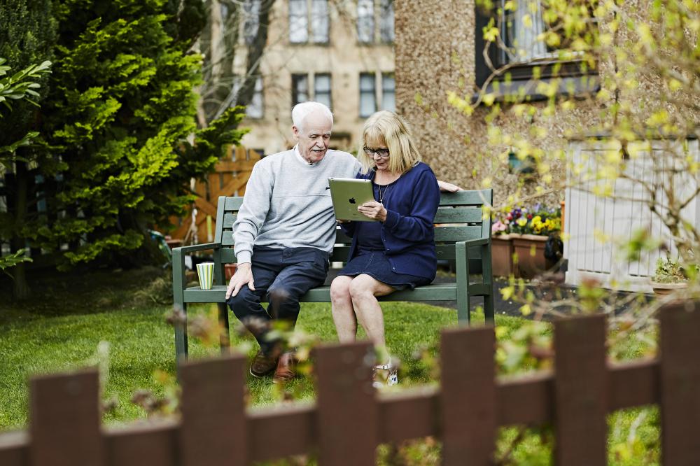 An older couple sit in the garden at Glentanar Court looking at a donated tablet computer and smiling